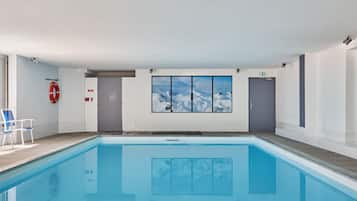 Ein Schwimmbad mit Blick auf schneebedeckte Berge durch ein großes Fenster.