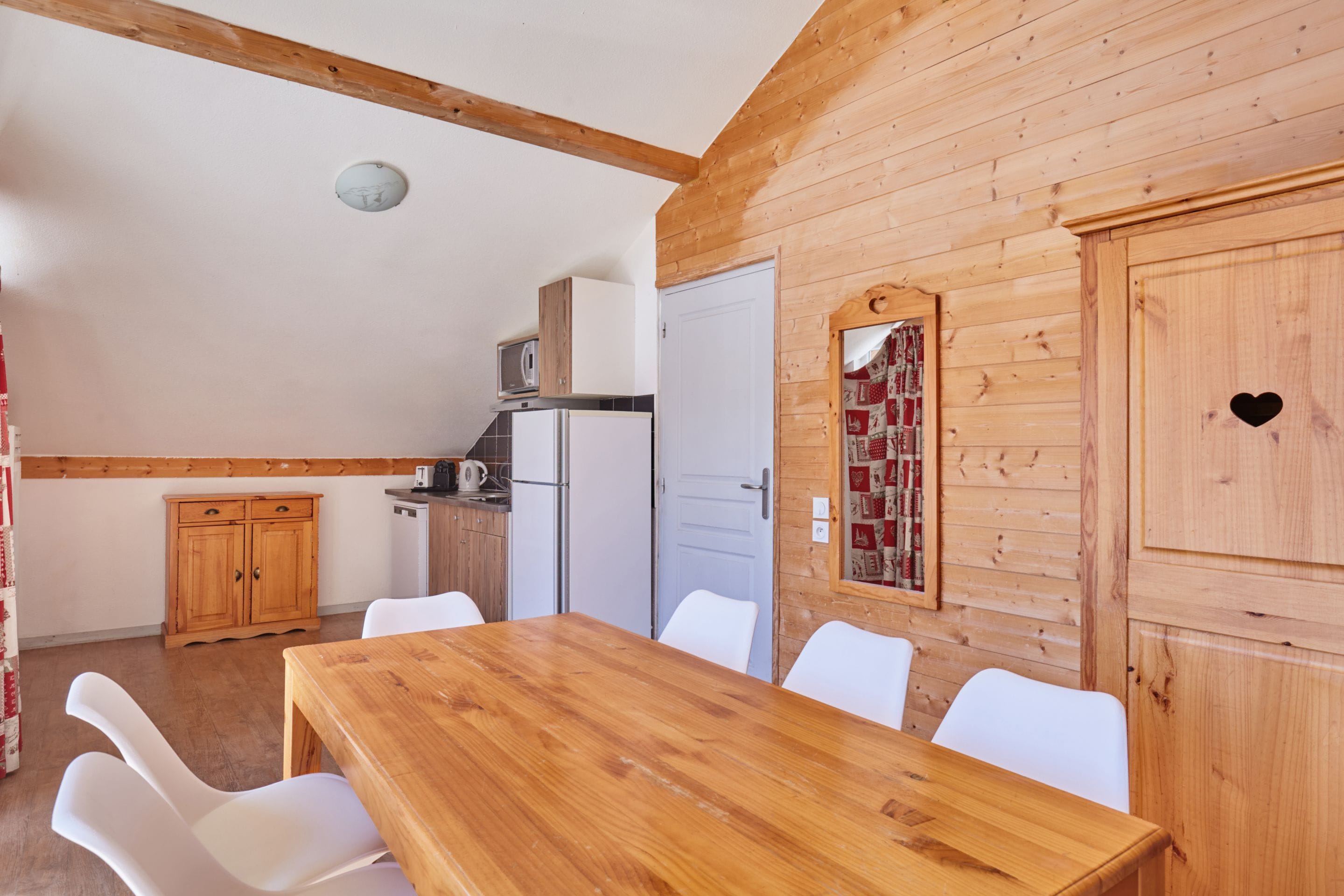 Een houten interieur met een eettafel, stoelen, een keukenhoek en een deur met een hartvormig uitsparing.