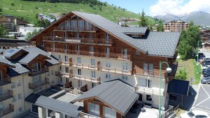 Un hôtel à plusieurs étages doté de balcons, une station de ski en arrière-plan et un paysage montagneux.