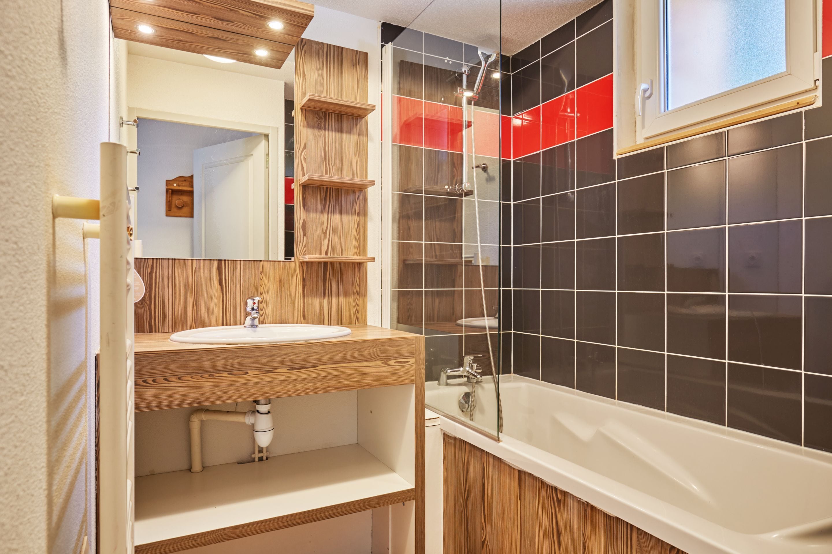 A modern bathroom with a wooden vanity, a large mirror, a bathtub, and a shower area.