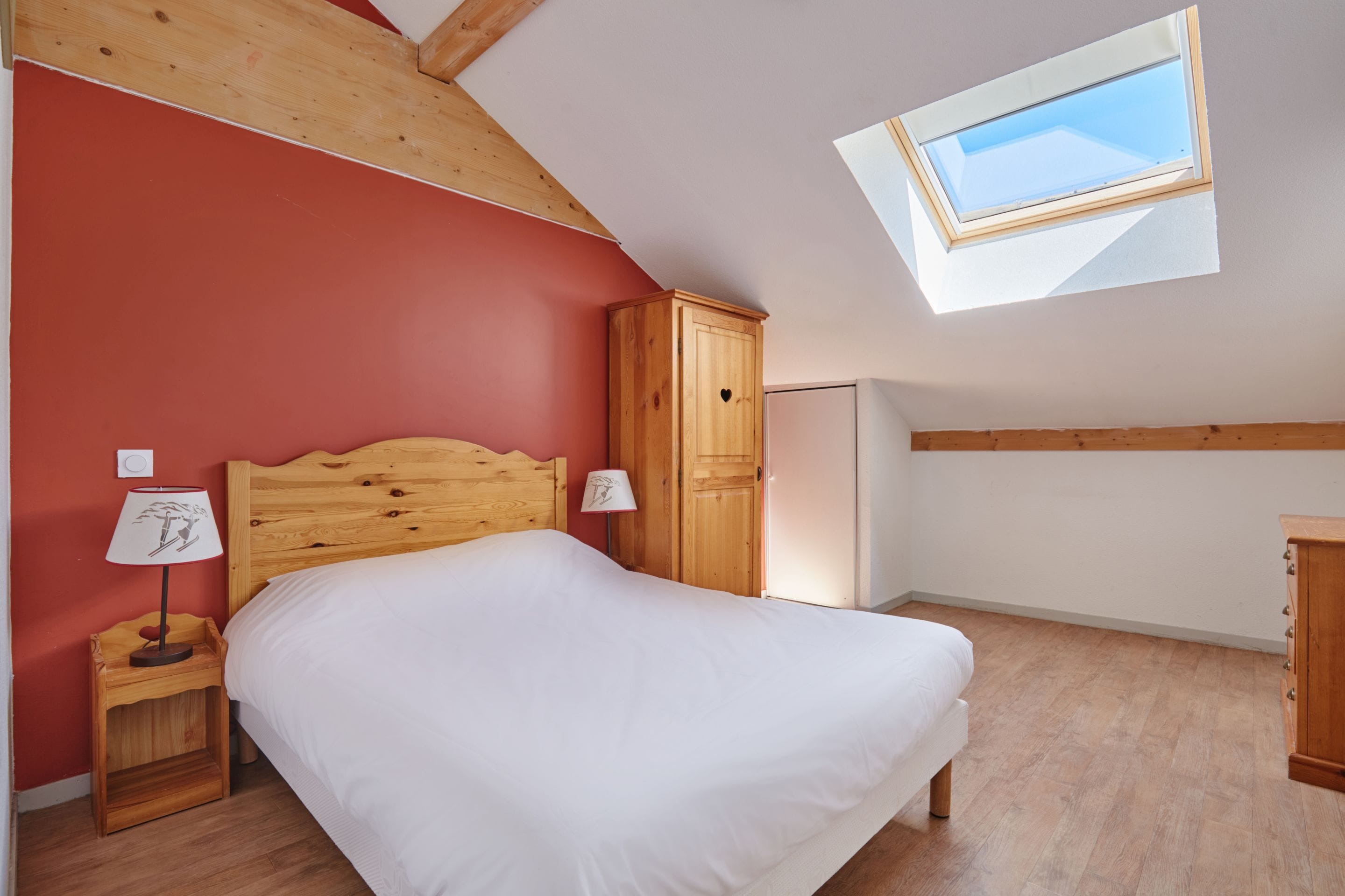 A bedroom with a bed, a wardrobe, a nightstand, a lamp, and a skylight.