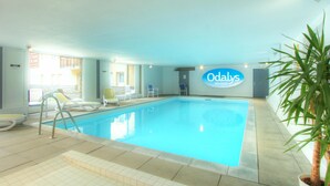 Une piscine intérieure avec des chaises longues et un panneau indiquant « Odalys Vacances ».