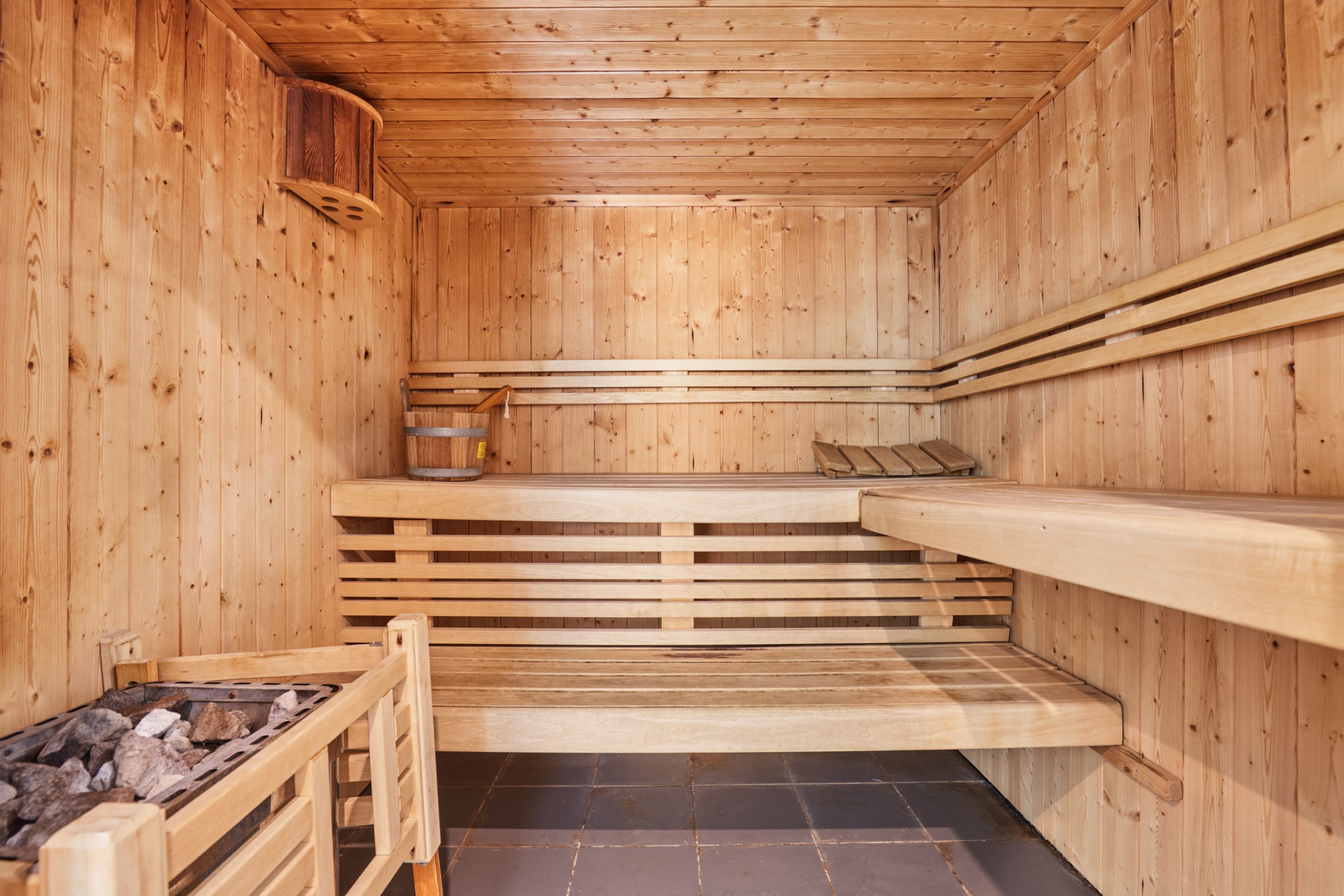 Una sauna con paredes y bancos de madera, suelo de piedra y un pequeño estante con objetos.