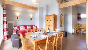 Un coin repas avec une table en bois dressée pour quatre personnes, un canapé rouge et un meuble avec deux portes.