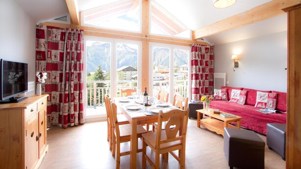 Un coin repas avec une table et des chaises en bois, un téléviseur posé sur un meuble et un canapé rouge.