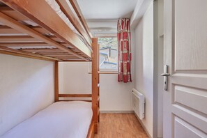 Een slaapkamer met stapelbed, raam, radiator en deur.