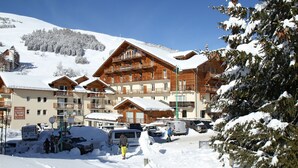Une station de ski enneigée, avec des bâtiments en bois, un télésiège et un ciel bleu dégagé.