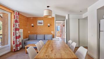 A modern interior with a wooden dining table, white chairs, a grey sofa, and a wooden wall.