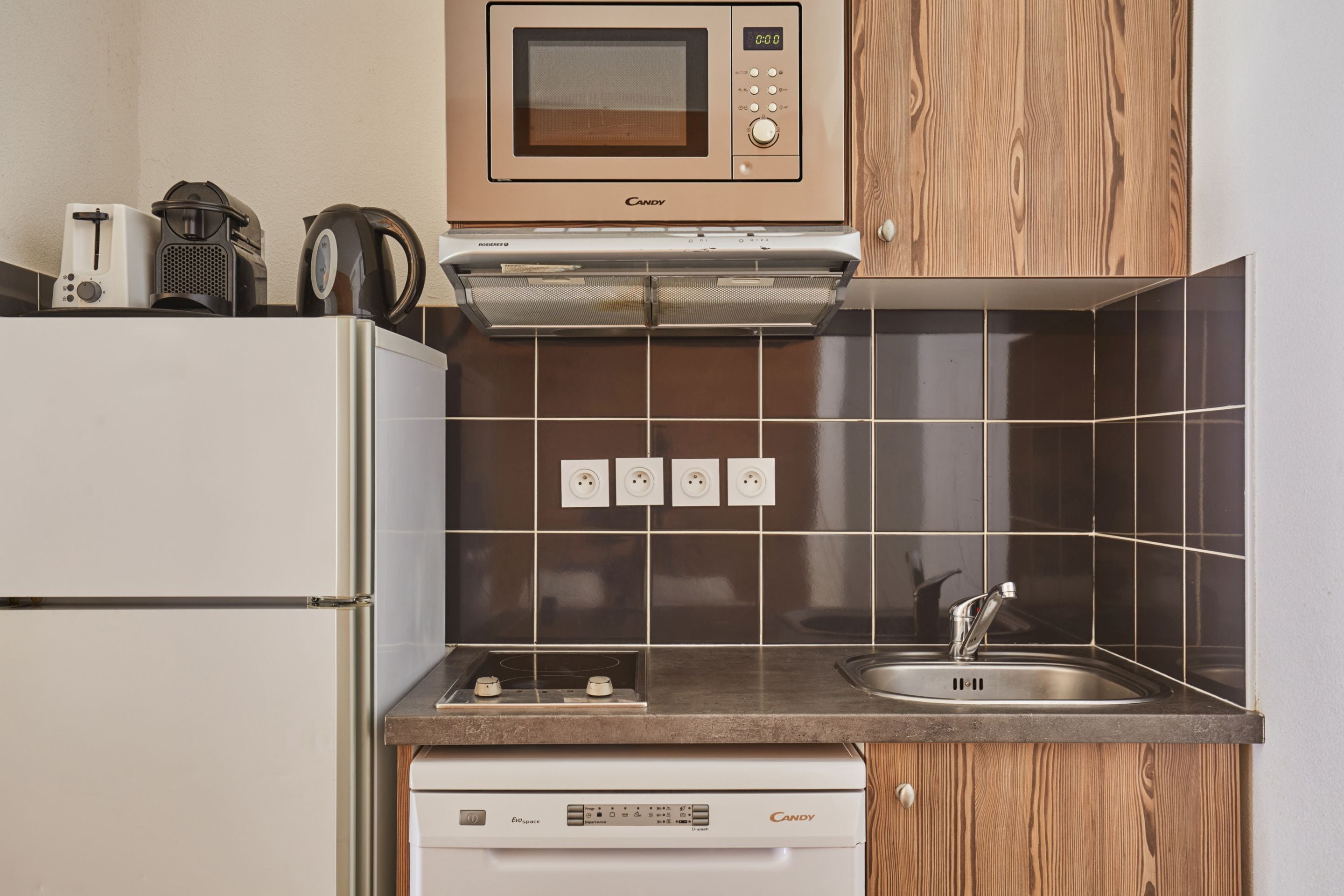 A compact kitchen with a microwave, toaster, kettle, and a dishwasher.