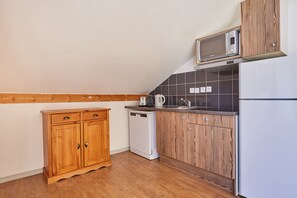 Una cocina compacta con armarios de madera, un lavavajillas blanco, un microondas y un refrigerador.
