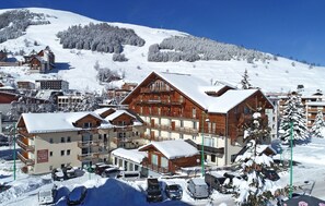 Une ville de montagne enneigée, avec des bâtiments en bois, dont un hôtel doté de balcons et d’une enseigne indiquant « Oberlies Residence L’Ours Blanc ».