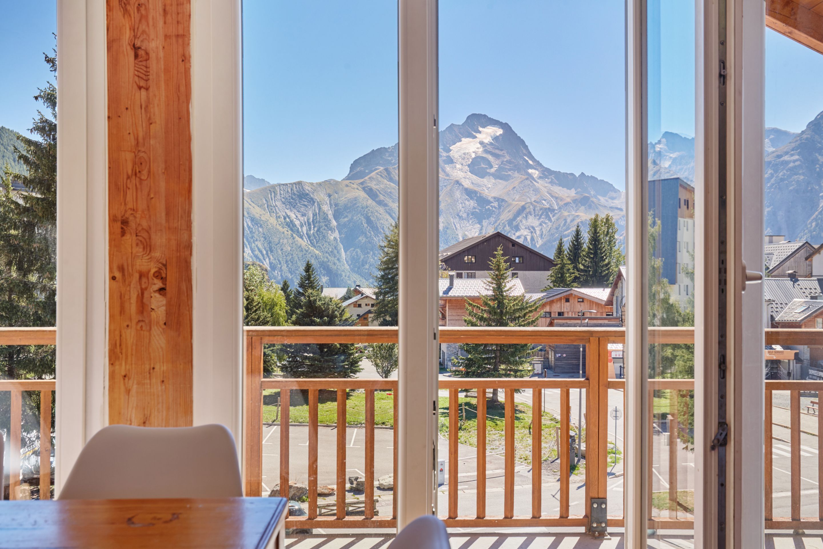 A room with a large window overlooking a mountain landscape, a wooden table, and a view of a building with a sign.