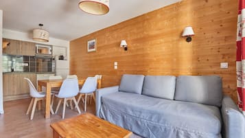 A modern living room with a wooden wall, a grey sofa, a wooden coffee table, and a kitchen area with a microwave and toaster.