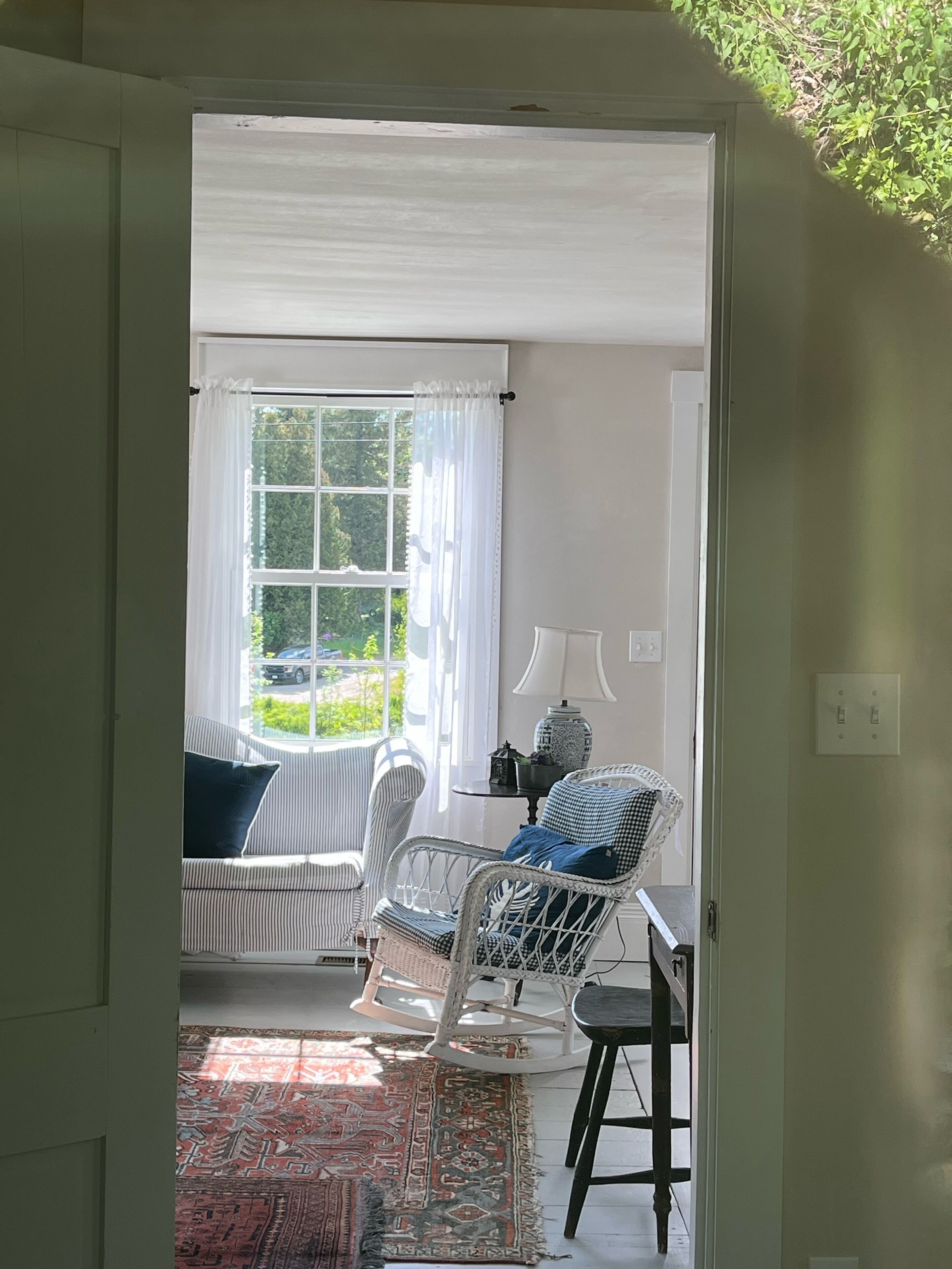 Une pièce avec une fenêtre, un canapé, une chaise, une petite table et un tapis.