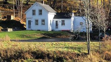 A white house with a chimney, a small shed, and a river in the foreground.