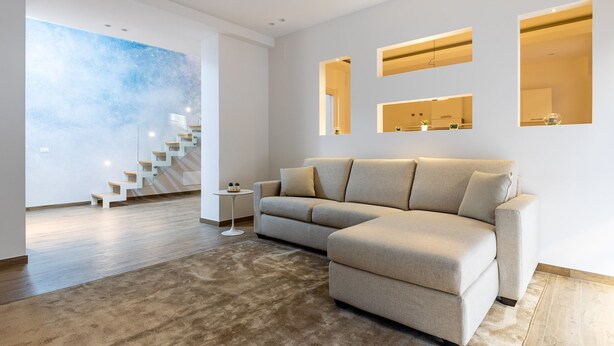 A modern living room with a sectional sofa, a staircase, and a large abstract wall mural. - Solemar Sicilia - Galleria Maqueda (Palermo)