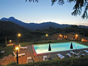 A swimming pool with lounge chairs and umbrellas, surrounded by a stone patio, with mountains in the background. - Agriturismo Summer (Gallicano)
