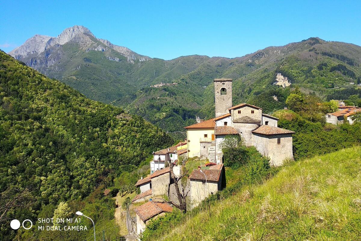 A historic stone building with a bell tower, surrounded by lush green hills and mountains.
