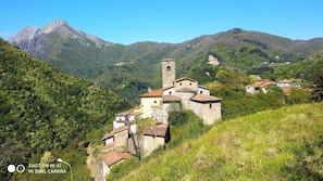 Un edificio histórico de piedra con una torre de campanas, rodeado de colinas y montañas verdes y exuberantes.
