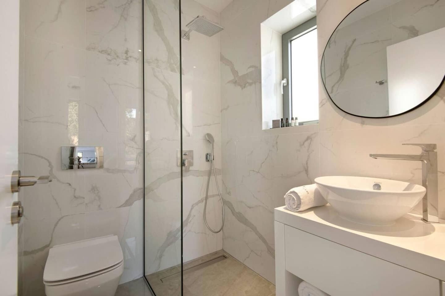Un baño moderno con ducha de vidrio, lavamanos blanco y retrete.