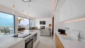 A modern kitchen with a large island, built-in oven, and a dining area with a view of the sea. - Golden Shore (Pegeia)