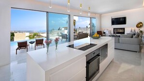 A modern kitchen with large windows, a central island, and a view of the sea. - Golden Shore (Pegeia)