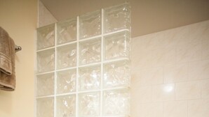 Un baño con inodoro, cabina de ducha de vidrio y suelo de baldosas.