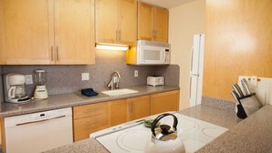 Una cocina con armarios de madera, microondas, refrigerador, lavavajillas y tetera.