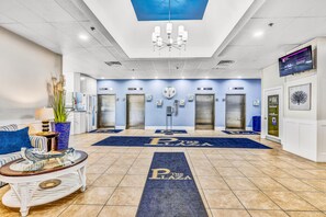 A hotel lobby with a reception desk, seating area, elevators, and a digital display.