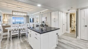 Une cuisine moderne avec des meubles blancs, un plan de travail en granit et un coin repas comprenant des chaises et une table, le tout dans des tons blancs.