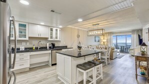 Une cuisine moderne avec des meubles blancs, un îlot central doté de tabourets et un coin repas offrant une vue agréable.