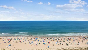 Une plage avec de nombreux parasols et beaucoup de monde, un ciel dégagé et l’océan.