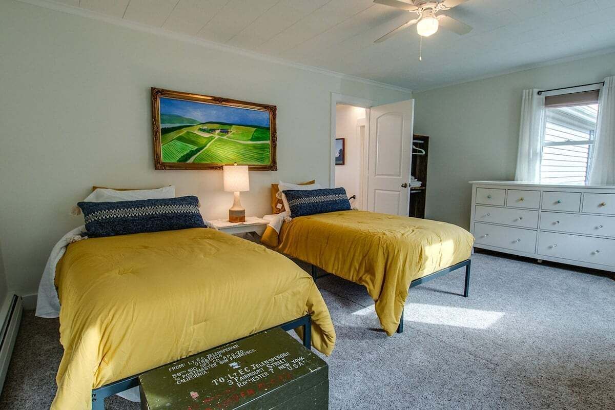A room with two beds, a painting on the wall, a dresser, and a window with curtains.