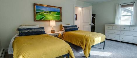 A room with two beds, a painting on the wall, a dresser, and a window with curtains.