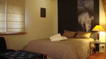 A hotel room with a bed, a nightstand with a lamp, a chair, and a large wall painting.