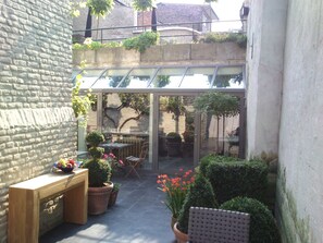 Une terrasse ensoleillée avec une véranda en verre, des plantes en pot et une table en bois.