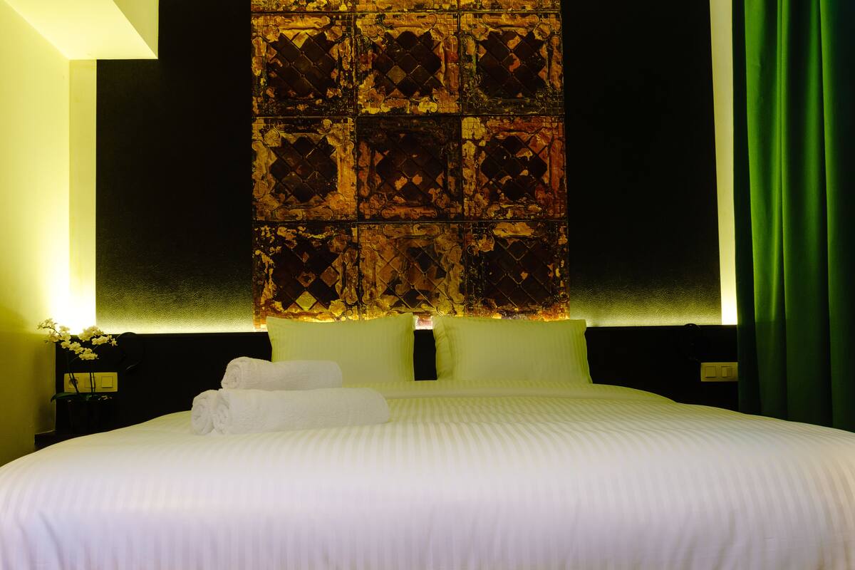 A neatly made bed with white linens, a decorative headboard, and a green curtain.