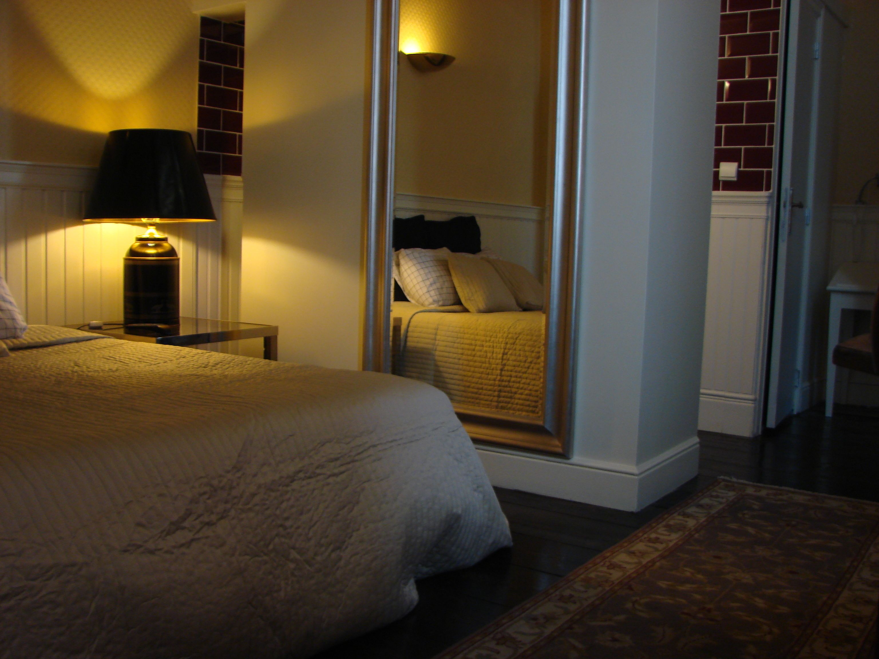 A hotel room with a bed, a nightstand, a lamp, and a mirror.