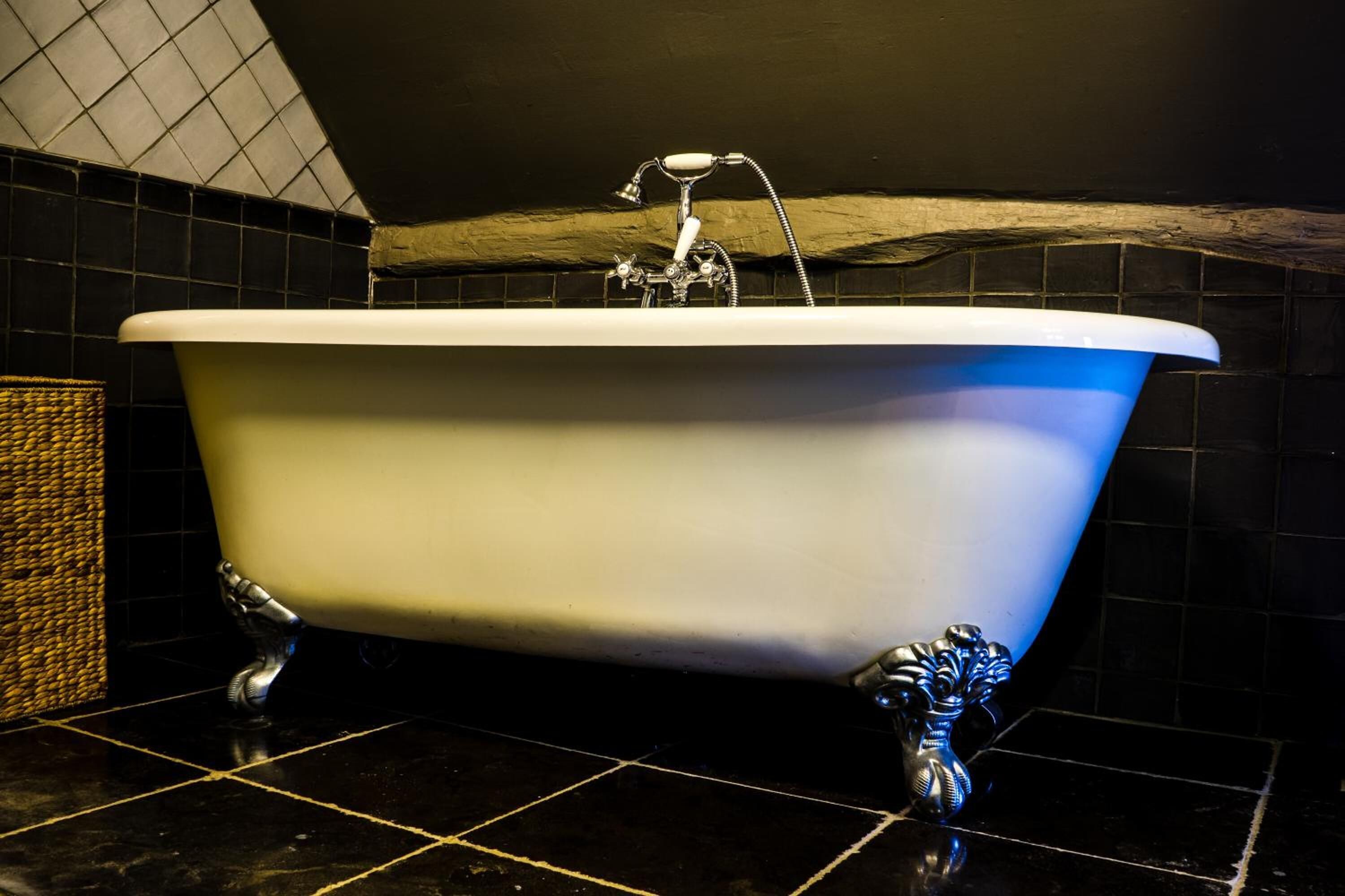 Una bañera de patas de león con diseño blanco y azul, frente a una pared de azulejos oscuros y una viga de madera.