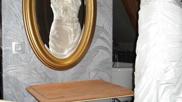 A room with a mirror, a mannequin in a white dress, a wooden table, and a red patterned sofa.