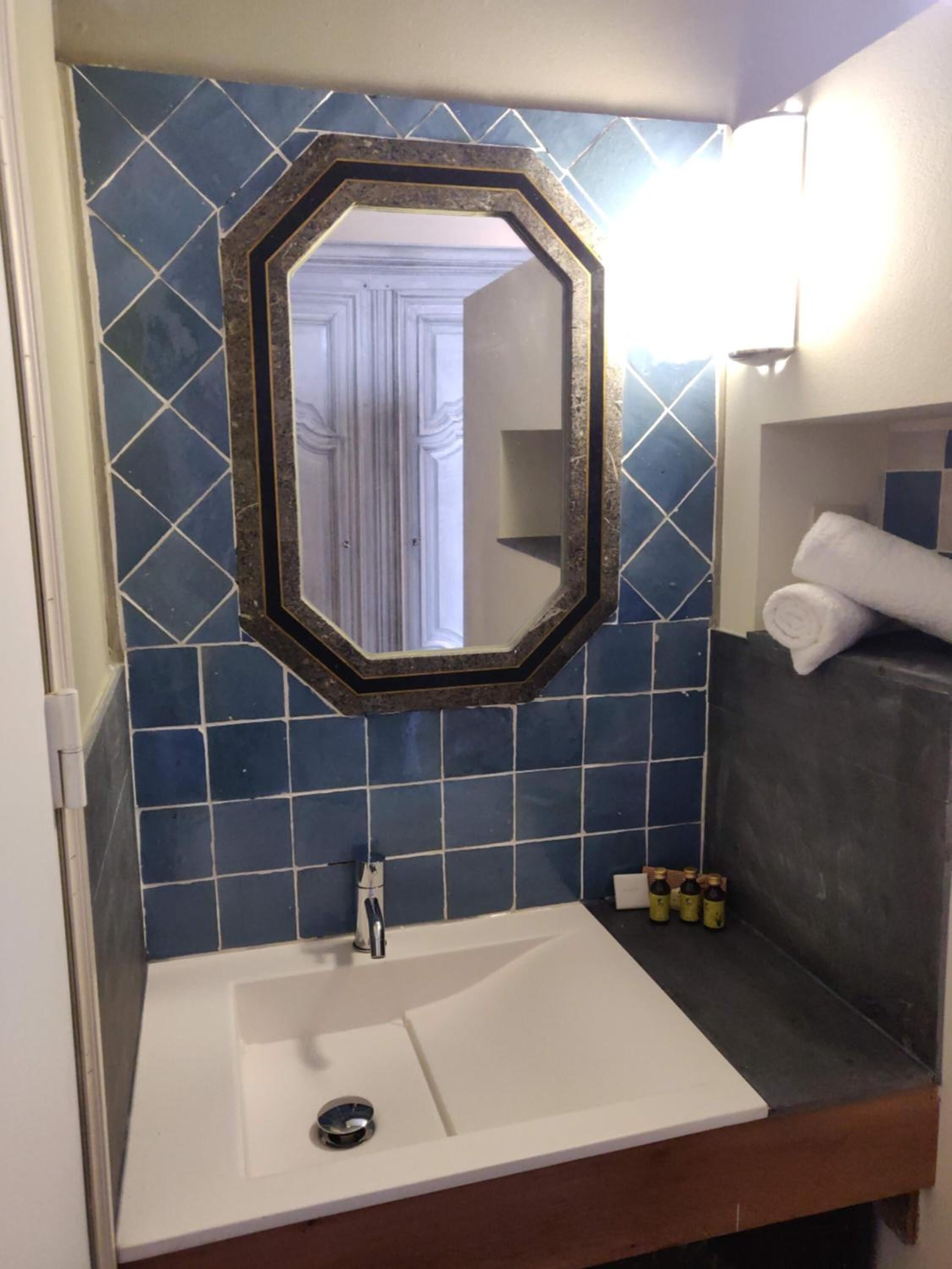 Un baño con un lavamanos blanco, un espejo con marco hexagonal y paredes cubiertas de azulejos azules.