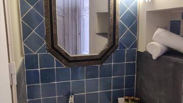 Un baño con un lavamanos blanco, un espejo con marco hexagonal y paredes cubiertas de azulejos azules.