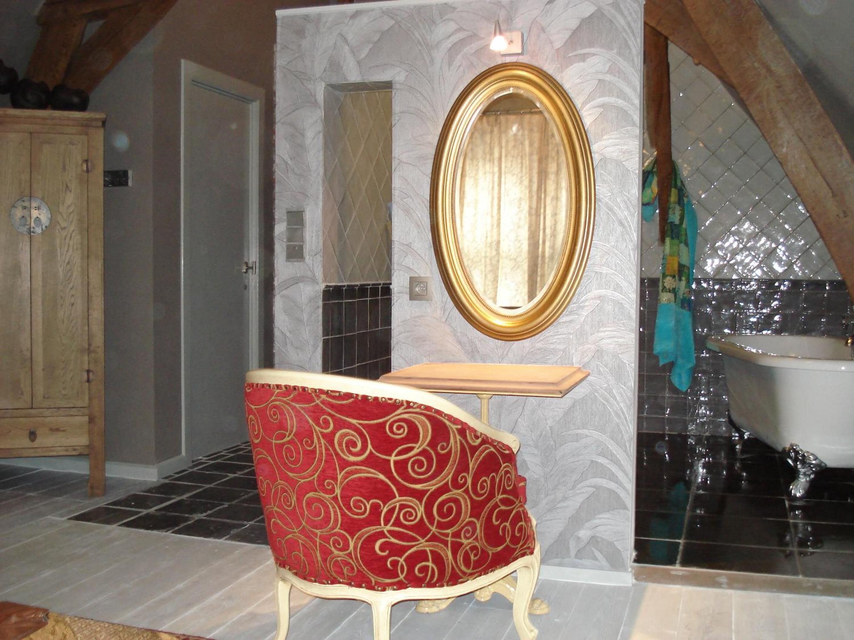 A bathroom with a bathtub, a vanity with a mirror, and a red upholstered chair.