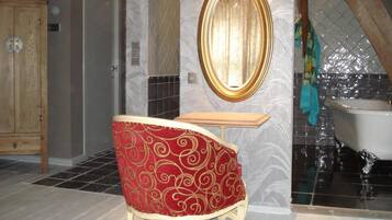 A bathroom with a bathtub, a vanity with a mirror, and a red upholstered chair.