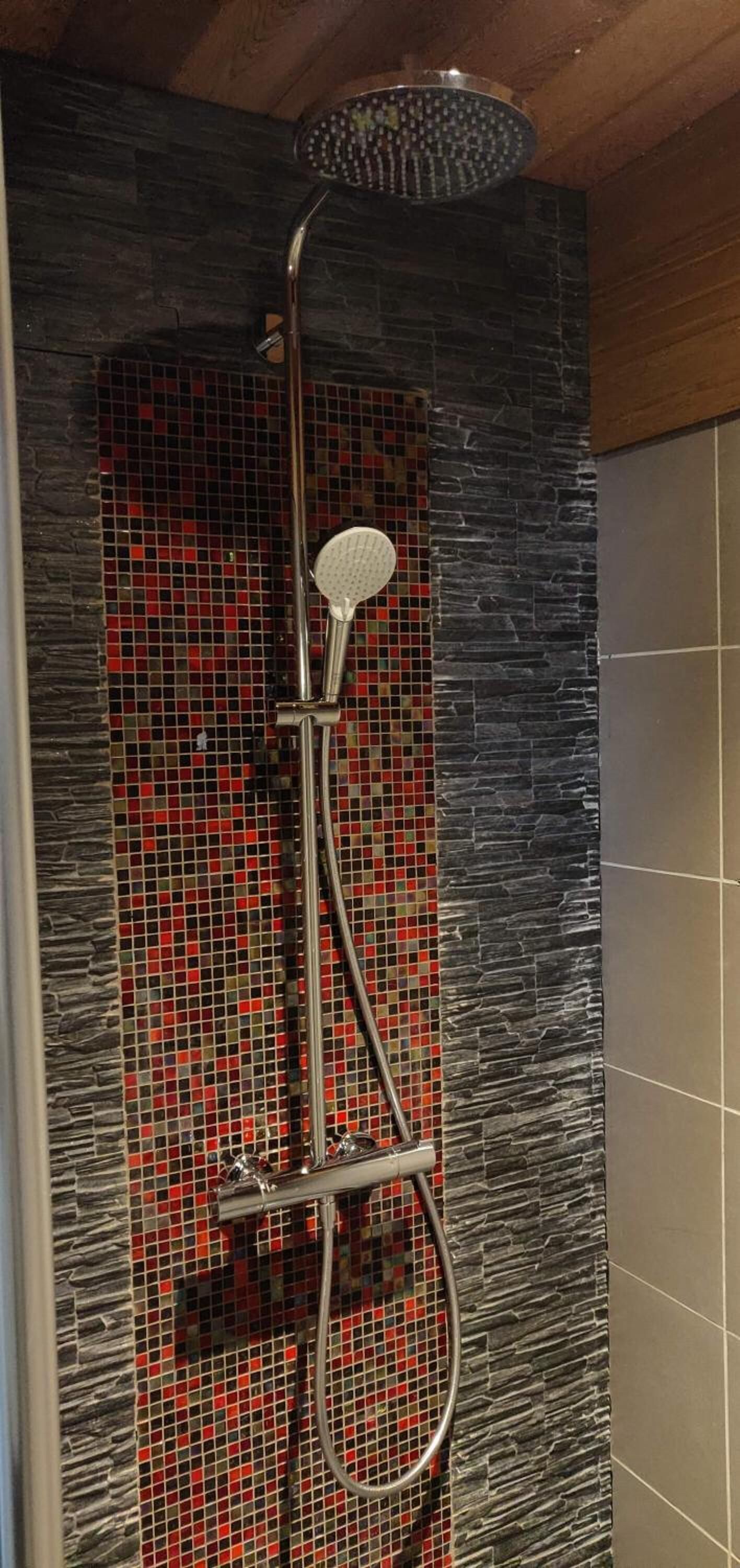 A shower with a rain showerhead and handheld showerhead, set against a mosaic tile wall.