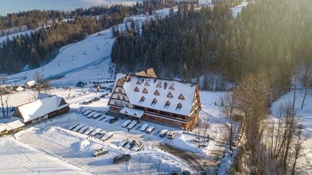 A lodge with a symmetrical roofline, multiple windows, and a parking area in a snowy landscape. - Hotel Góralski Wellness & SPA (Poronin)