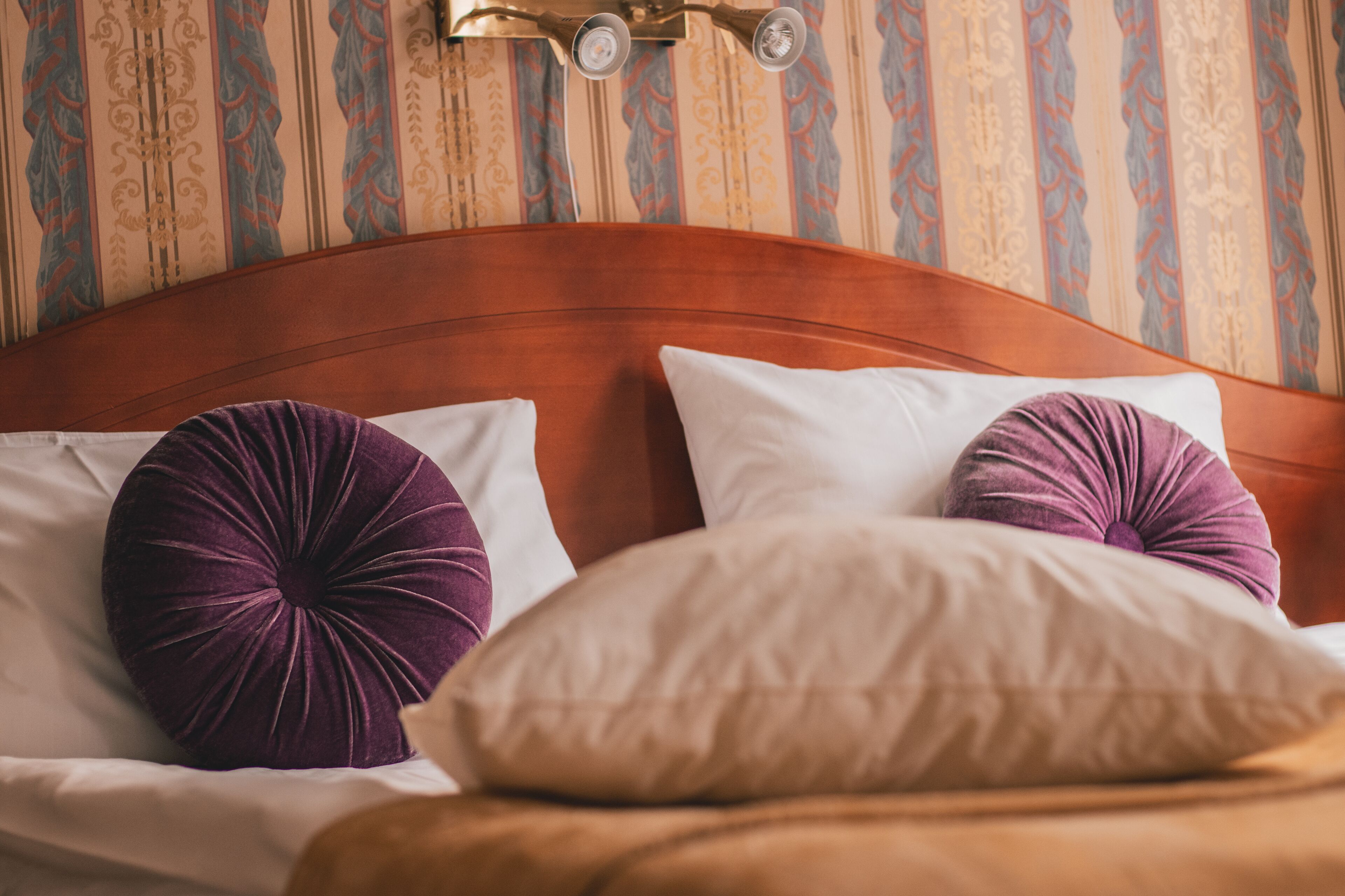A bed with a wooden headboard, two purple pillows, and a beige pillow.