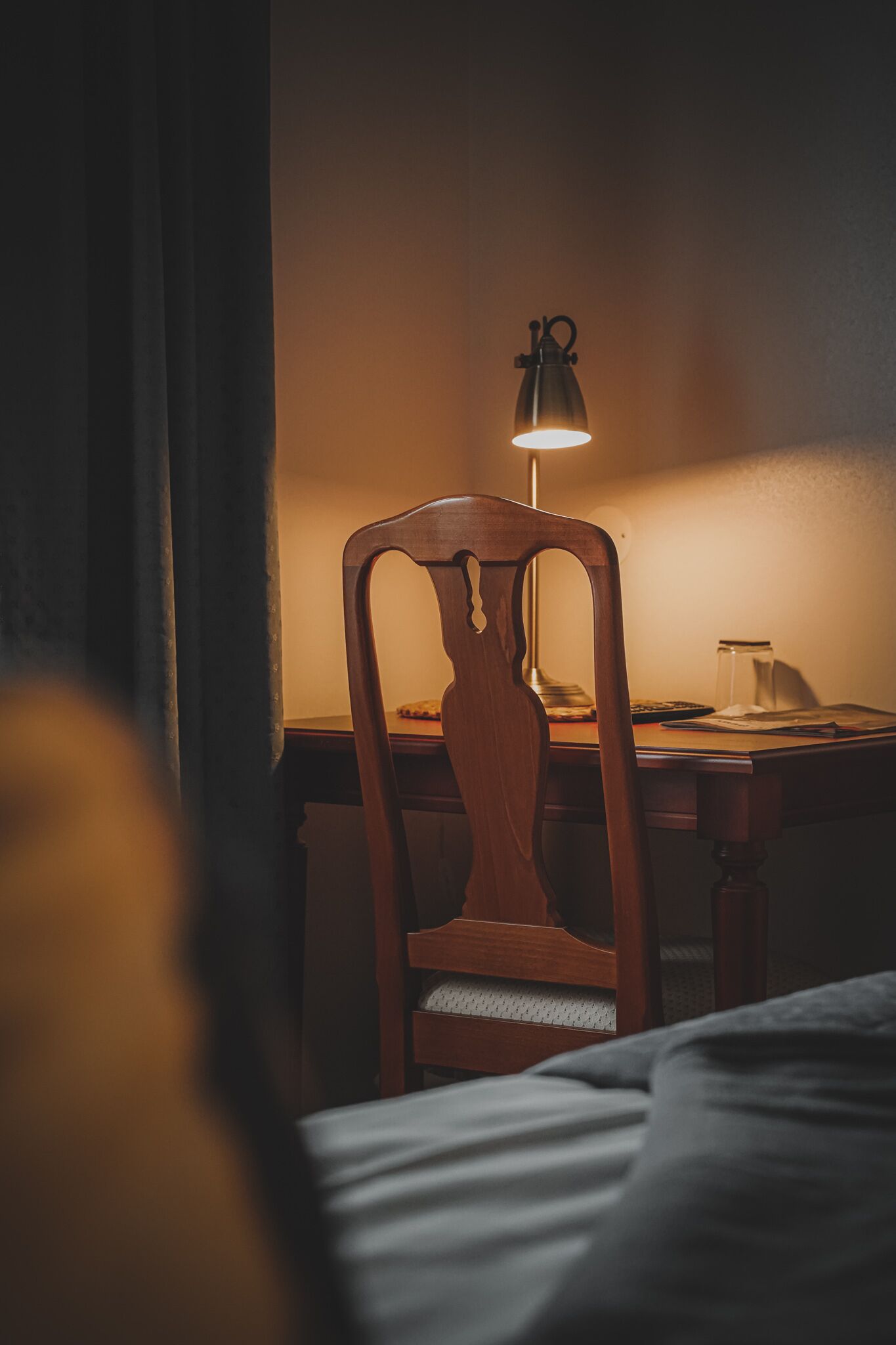 Ein Holzsessel mit einer Metalllampe auf einem Schreibtisch in einem schwach beleuchteten Raum.