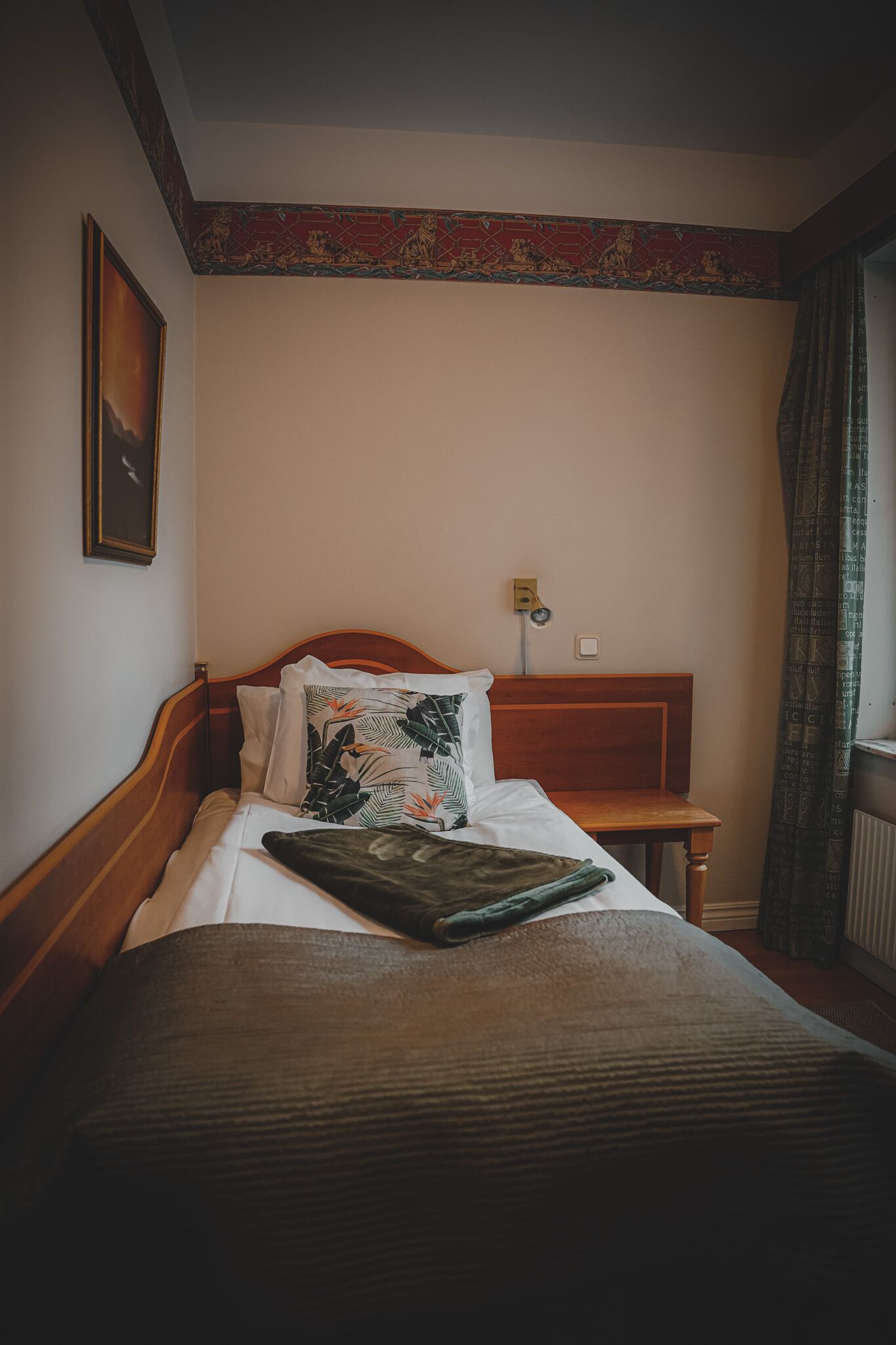 Cama bem arrumada com cabeceira de madeira, mesa de cabeceira e luminária fixada na parede.