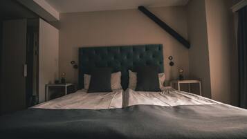 A bedroom with a tufted headboard, two bedside tables with lamps, and a large bed with a dark blanket.